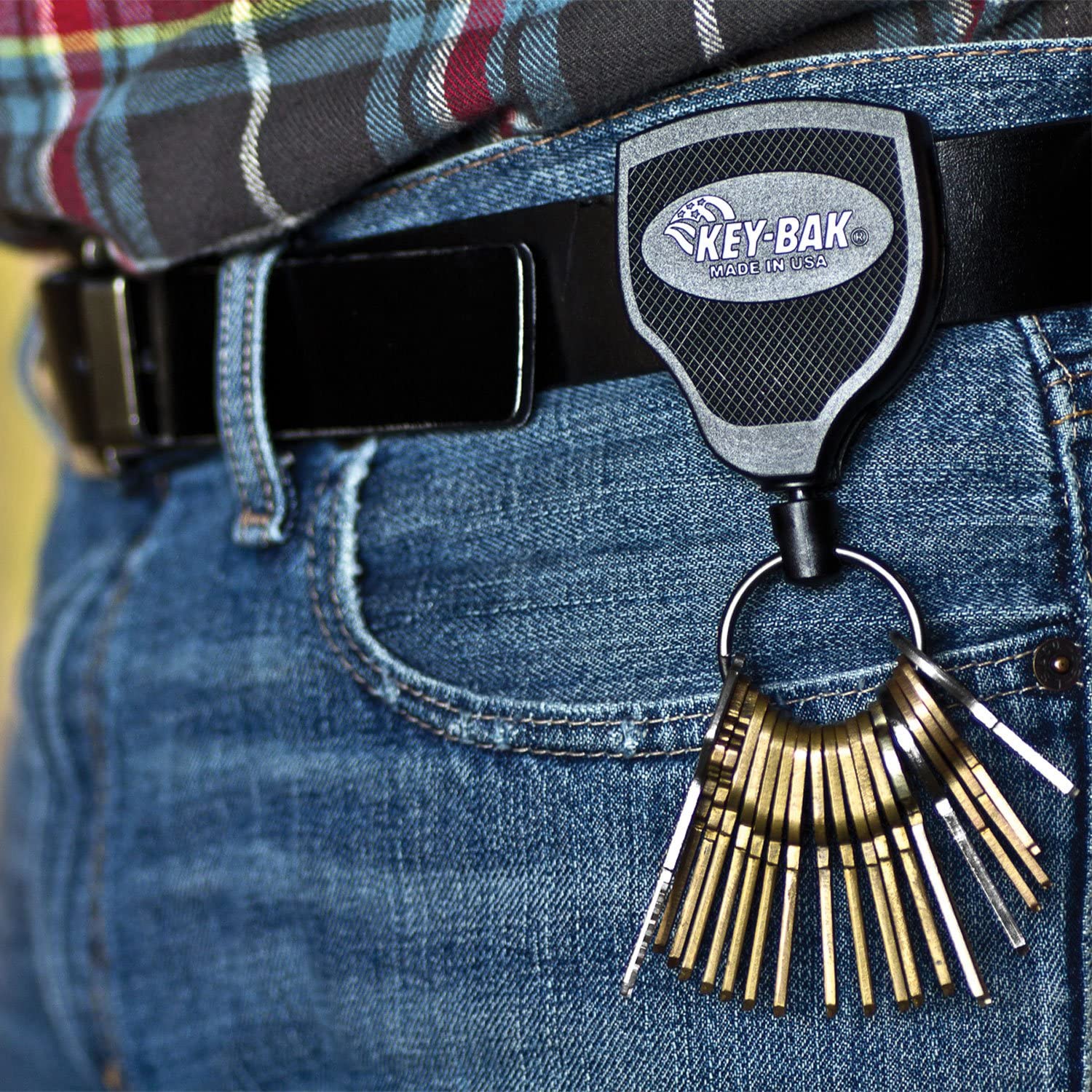 Ein KEY-BAK Key-Bak Schlüsselhalter mit einem robusten Gurtclip ist an einem schwarzen Gürtel an einer blauen Jeans befestigt und hält mehrere Schlüssel sicher fest. Ein kariertes Hemd ist in der Szene teilweise sichtbar.