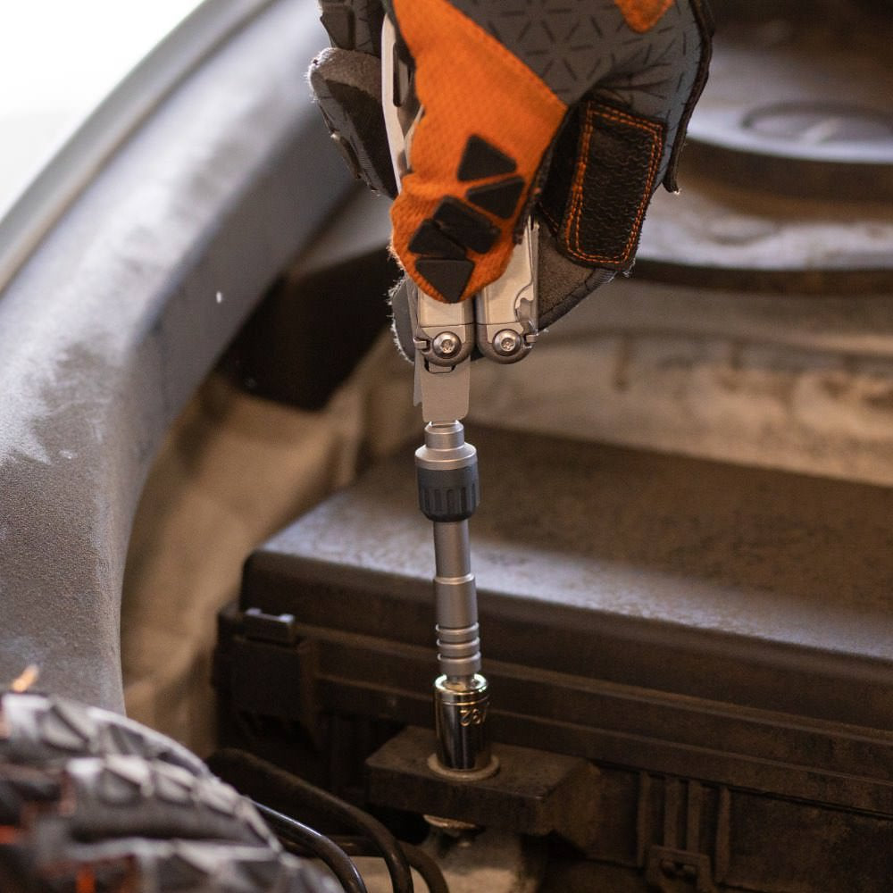 Eine behandschuhte Hand benutzt den LEATHERMAN RATCHET DRIVER mit einem Steckschlüsselaufsatz, um eine Schraube an einem Auto-Motorteil festzuziehen.