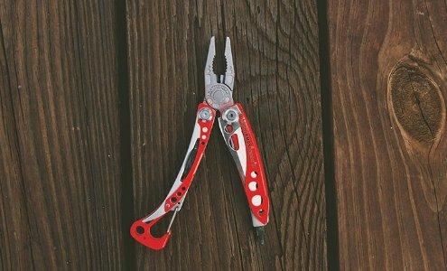 Ein LEATHERMAN Skeletool RX Multitool in Rot und Silber, dargestellt mit einer offenen Zange auf einer Holzoberfläche mit sichtbarer Maserung und Ästen.