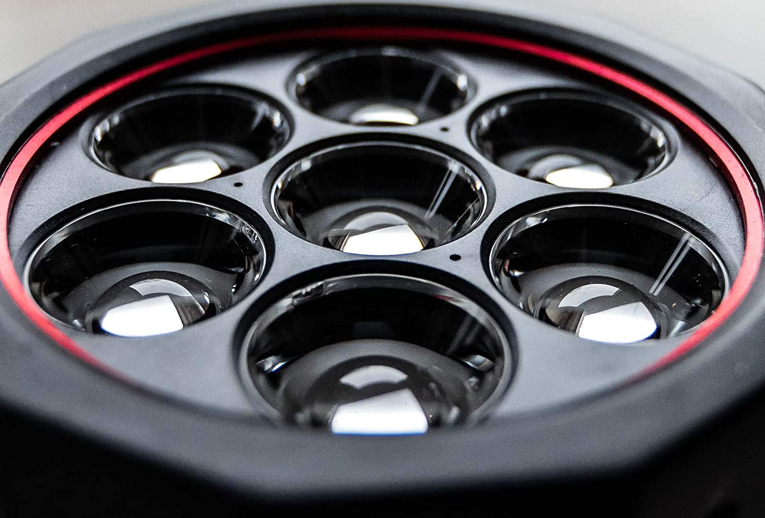 Nahaufnahme von sieben kreisförmigen Linsenelementen in sechseckiger Anordnung, umrandet von schwarzen und roten Ringen, die das Licht reflektieren - ein Hinweis auf das leistungsstarke Design der LEDLENSER Lampe X21R.