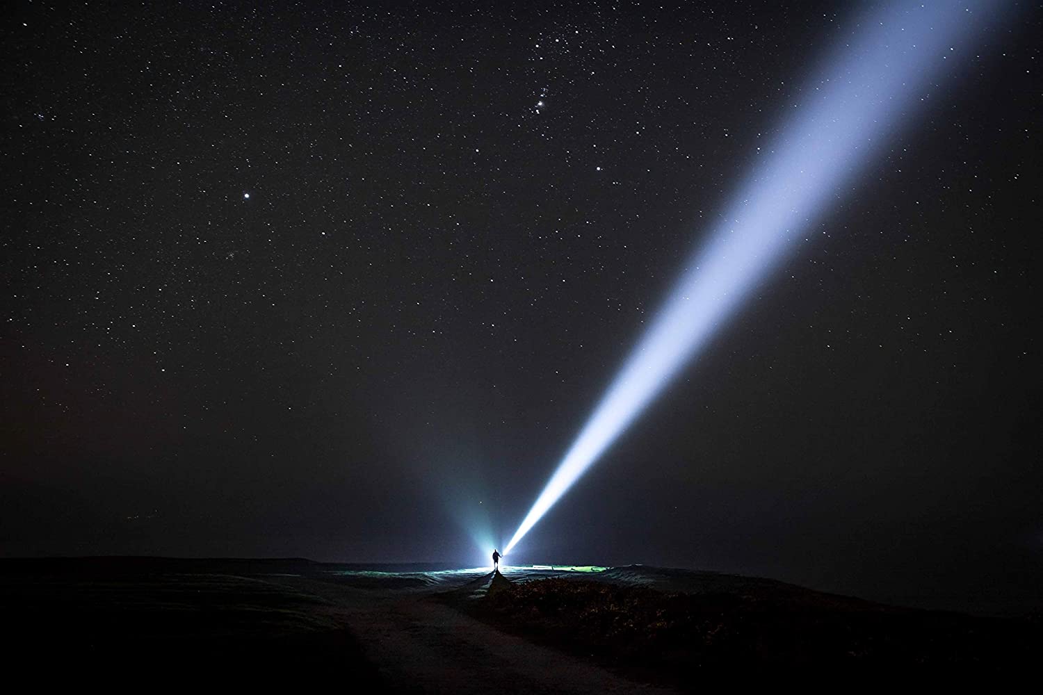Nachts unter dem Sternenhimmel leuchtet eine Person mit der LEDLENSER Lampe X21R schräg nach oben, erhellt die Landschaft und durchbricht die Dunkelheit.