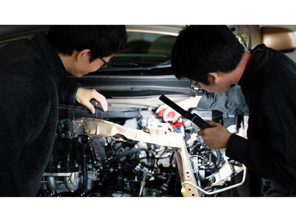 Zwei Personen inspizieren einen Automotor - die eine leuchtet mit einer LEDLENSER W7R Work die Motorkomponenten aus, während die andere auf etwas im Motorraum zeigt.