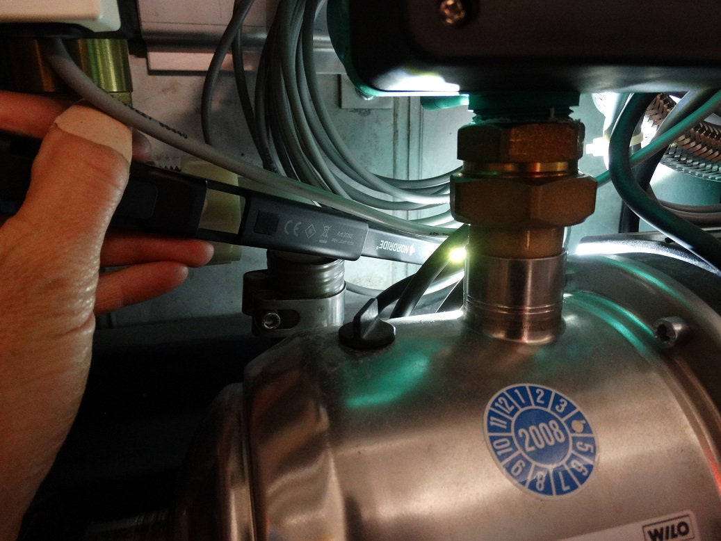 Eine Hand prüft mit einem Diagnosewerkzeug die Verdrahtung einer Industriepumpe mit dem Aufkleber "2008", während die NORDRIDE Nordride Arbeitslampe Pen Light Flex Kabel und Anschlüsse beleuchtet.