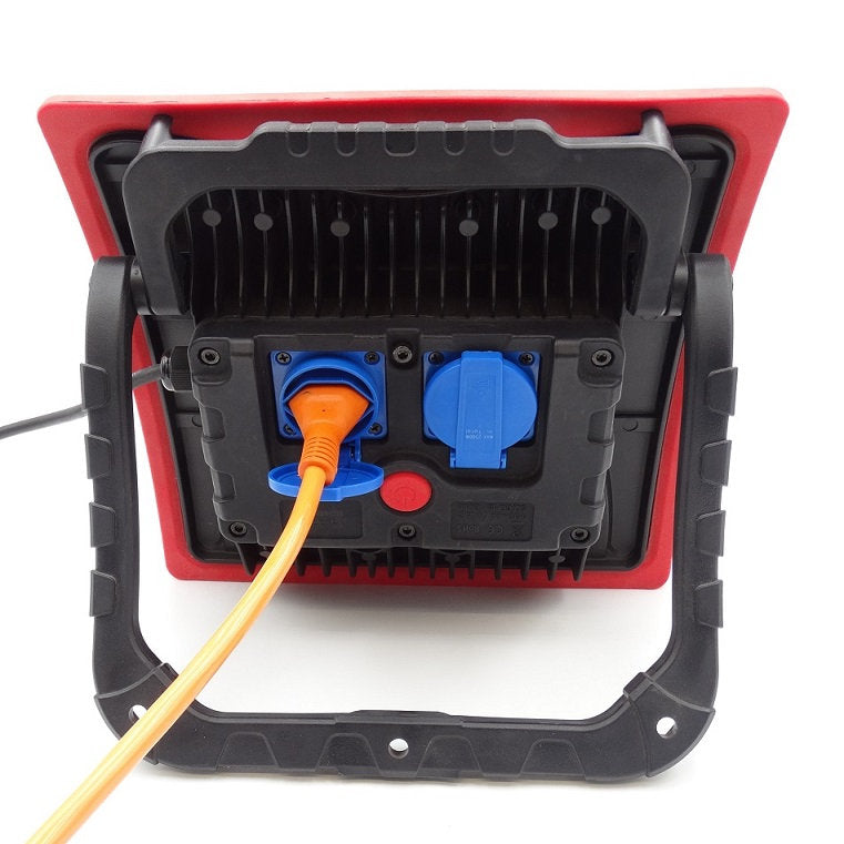 Eine Nahaufnahme der Rückseite des NORDRIDE Nordride Arbeitsstrahler Power Light 60W zeigt einen schwarz-roten Rahmen, zwei blaue Steckdosen und ein orangefarbenes Kabel, das eingesteckt ist und eine leistungsstarke Beleuchtung mit 5000 Lumen liefert.