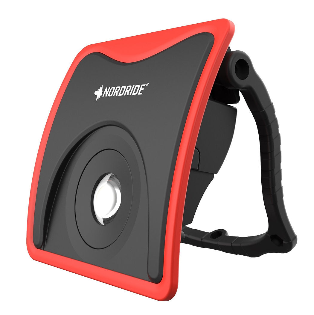 Der NORDRIDE Arbeitsstrahler Slim Power 20W ist ein schwarz-roter, wiederaufladbarer LED-Arbeitsstrahler mit einem Griff, der mit dem NORDRIDE-Logo versehen ist, einer zentralen, runden LED-Linse und einem verstellbaren Ständer für vielseitige Beleuchtung.