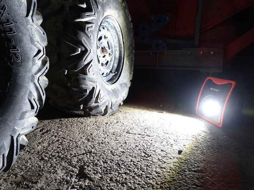 Der NORDRIDE Nordride Arbeitsstrahler Slim Power 20W beleuchtet hell den Boden neben großen, robusten Traktorreifen in einem schwach beleuchteten Bereich und hebt die strukturierte Betonoberfläche hervor.