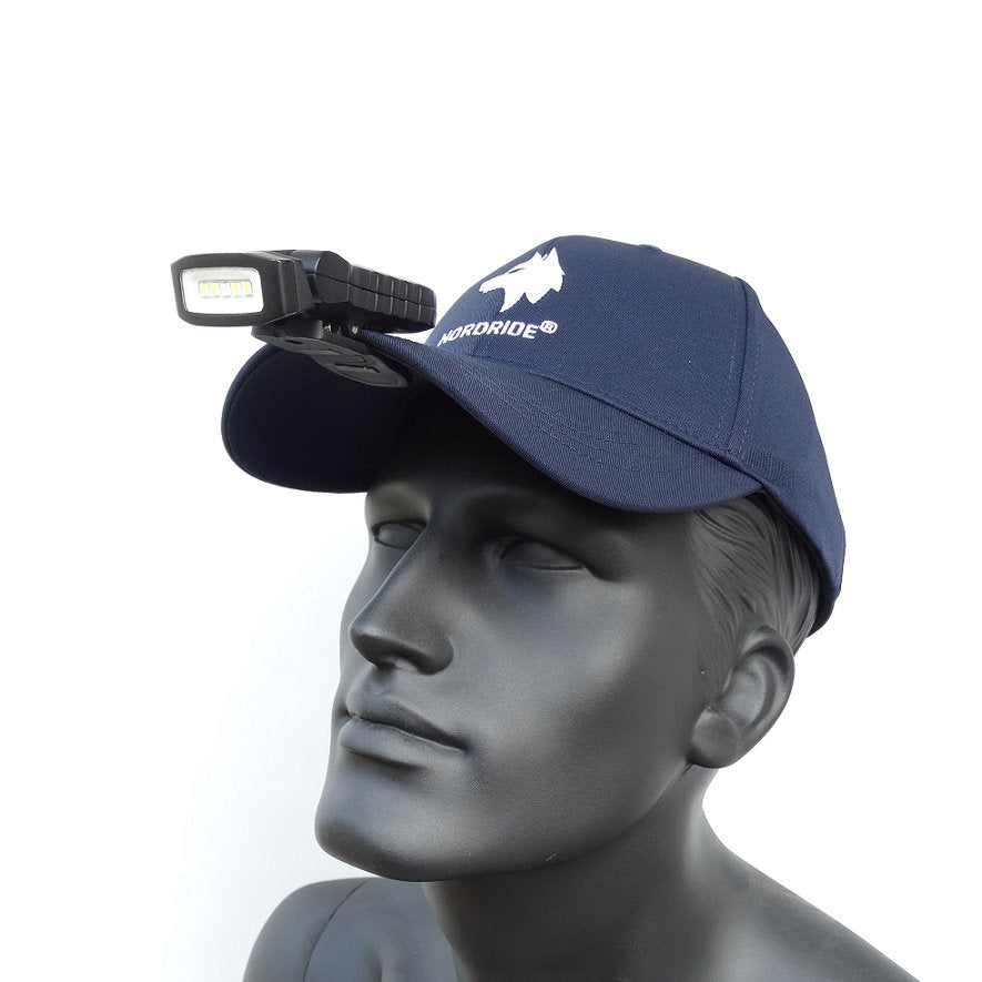 Eine Schaufensterpuppe trägt eine marineblaue Mütze mit Berg-Logo und einer NORDRIDE Nordride Clipleuchte Scout Red LED-Stirnlampe, die an der Krempe befestigt ist, vor einem schlichten weißen Hintergrund.