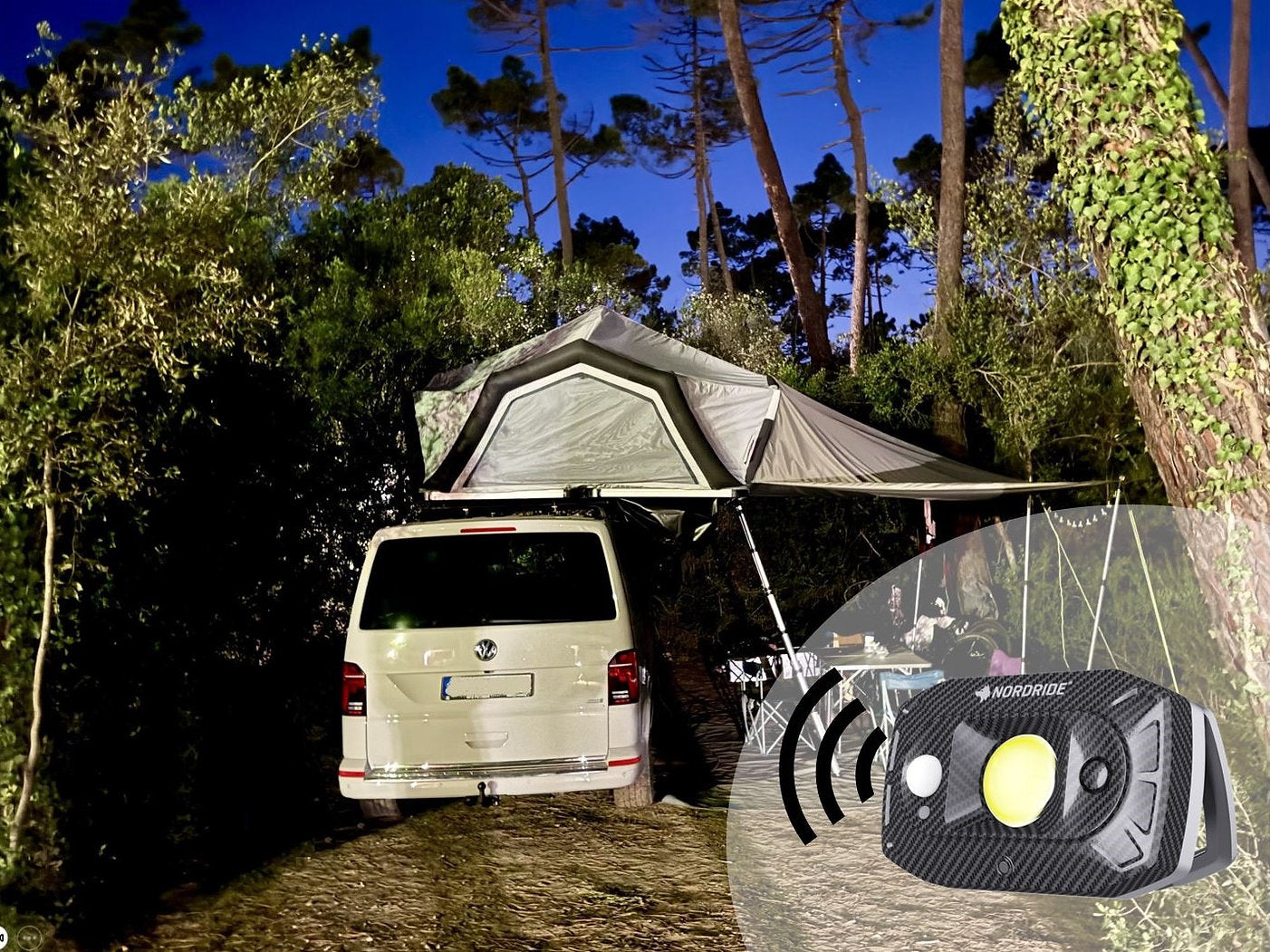 Ein weißes Wohnmobil mit einem Dachzelt steht in der Abenddämmerung auf einem bewaldeten Campingplatz in der Nähe von Tisch und Stühlen. Ein Einsatz hebt den NORDRIDE Nordride Flutlichtstrahler Guard hervor, der mit Sicherheitsfunktionen und dem charakteristischen gelben Knopf mit Signalwellen ausgestattet ist.