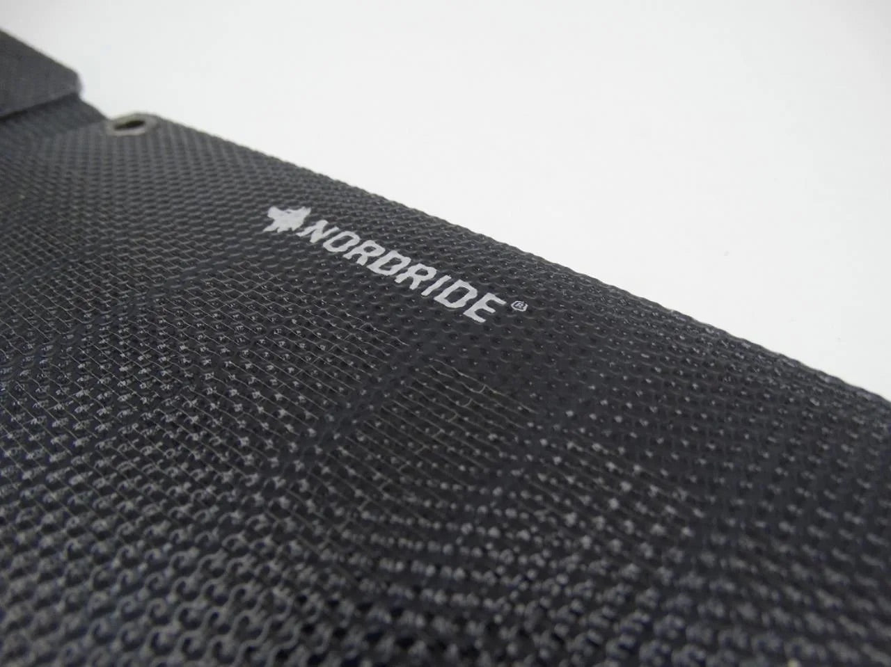 Nahaufnahme der strukturierten schwarzen Oberfläche des NORDRIDE SOLAR PULSE 24W mit dem NORDRIDE-Branding und dem Baumlogo in Weiß, das das Materialmuster zeigt und auf die fortschrittliche Technologie des mobilen Solarladegeräts hinweist.
