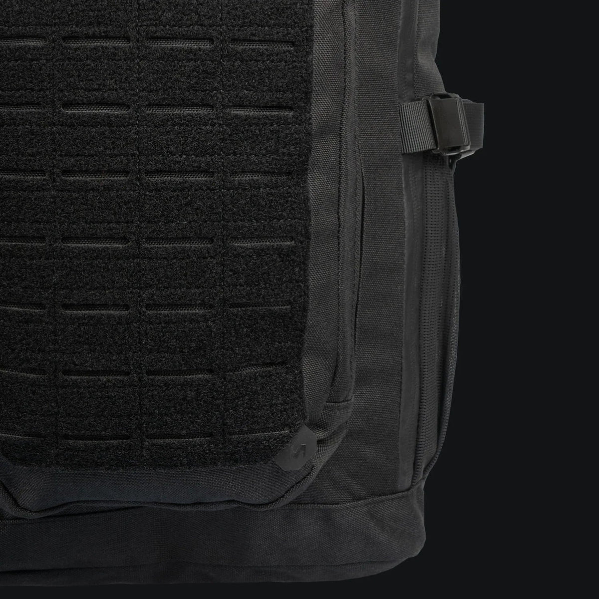 Die Nahaufnahme des STOIRM 25L Tactical Pack GEN2 von STOIRM hebt die lasergeschnittene MOLLE-Frontplatte, den seitlichen Reißverschluss und den verstellbaren rechten Gurt hervor, alles vor einem dunklen Hintergrund.
