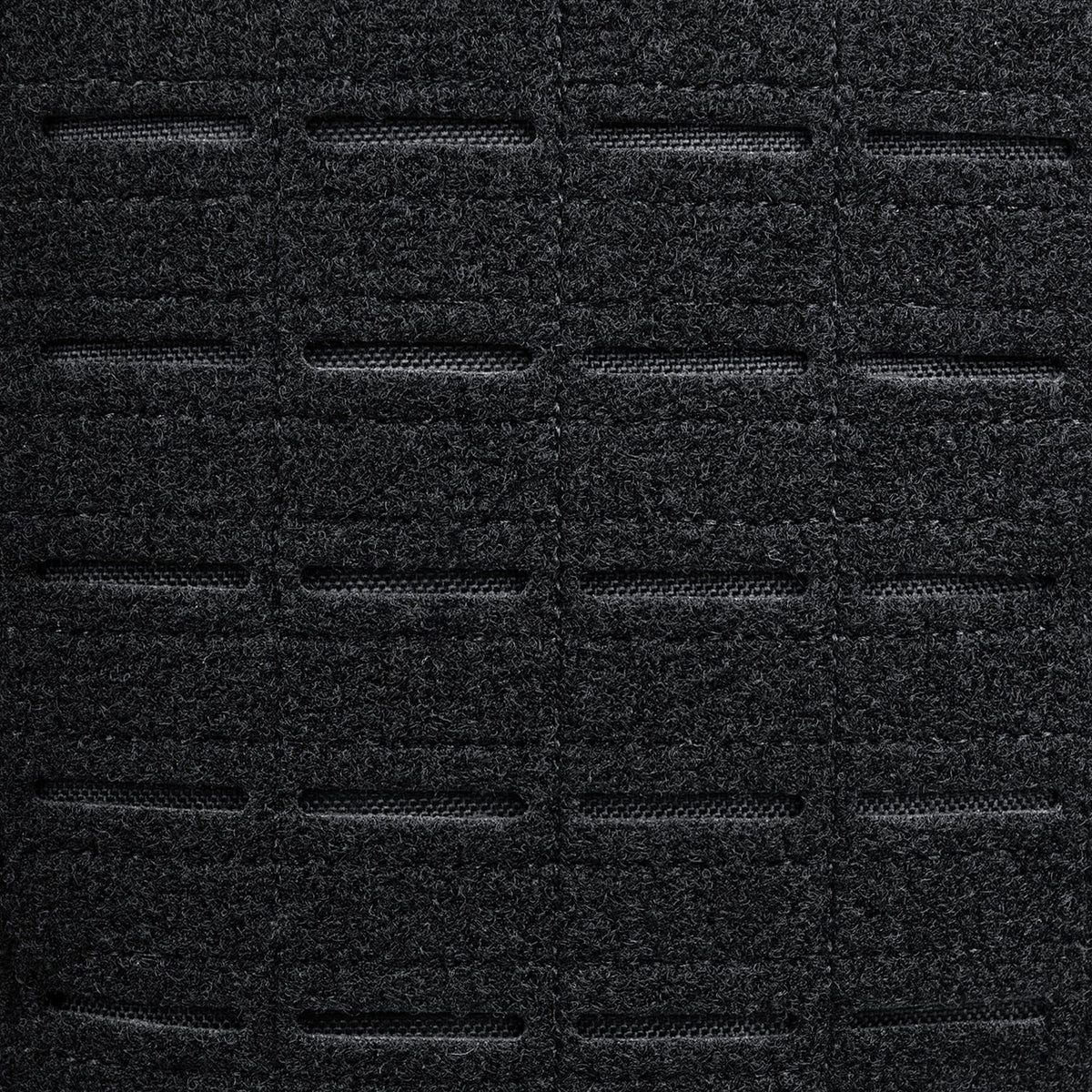 Nahaufnahme des schwarzen, strukturierten Gewebes des STOIRM 25L Tactical Pack GEN2 mit gleichmäßig verteilten horizontalen Schlitzen in einem Gittermuster, die das robuste Design ideal für den Outdoor- und taktischen Einsatz zeigen.