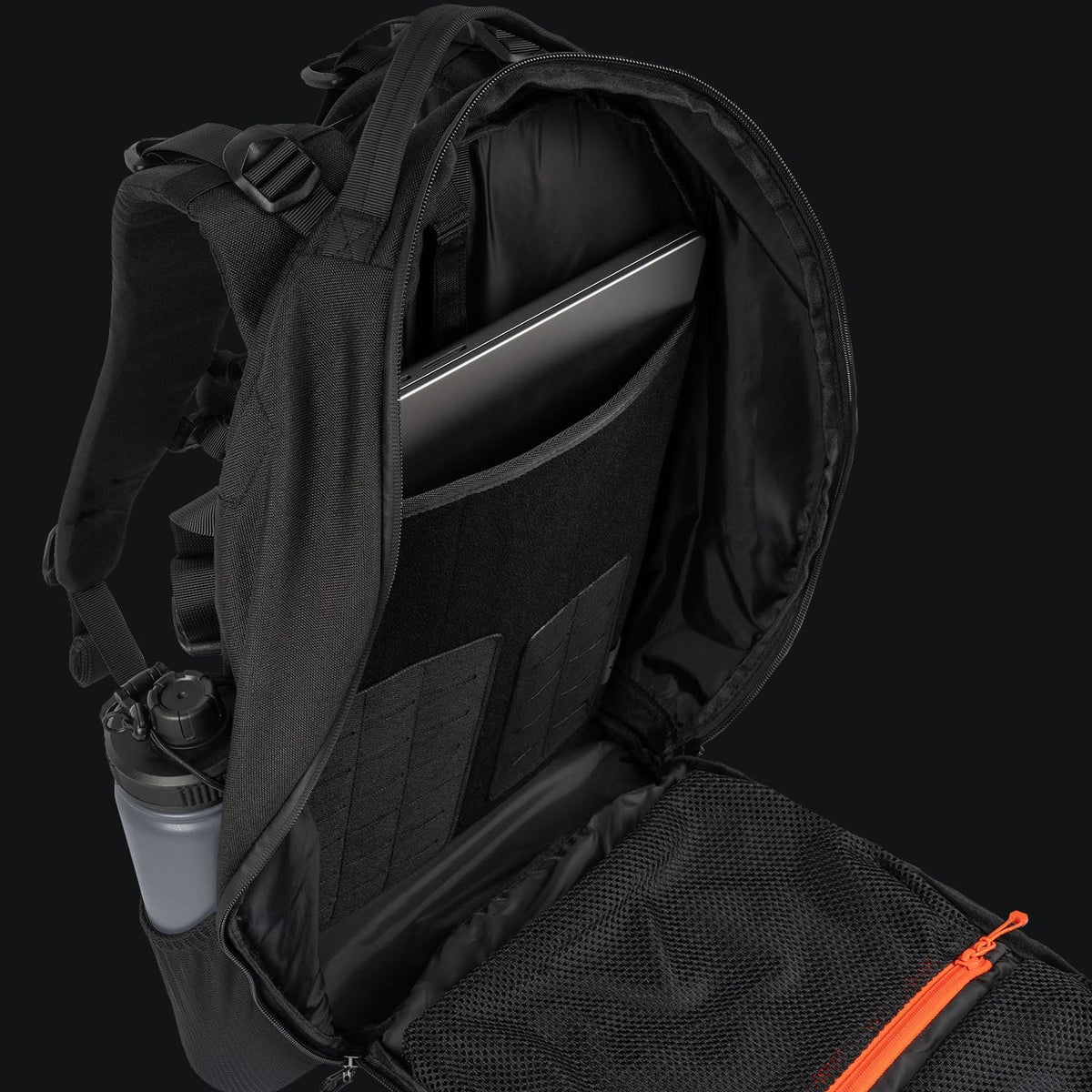 Ein schwarzer STOIRM 25L Tactical Pack GEN2 von STOIRM ist geöffnet und zeigt einen Laptop in seinem gepolsterten Fach. Eine Wasserflasche befindet sich in der Seitentasche und eine orangefarbene Netztasche mit Reißverschluss befindet sich im Hauptfach, alles vor einem dunklen Hintergrund.