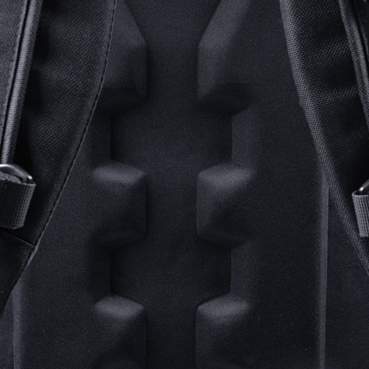 Nahaufnahme des schwarz gepolsterten Rückenteils eines STOIRM 25L Tactical Pack GEN2, mit erhabenen rechteckigen Schaumstoffabschnitten und strukturiertem Gewebe, wobei ein Teil der Schultergurte sichtbar ist - ein Markenzeichen dieses STOIRM-Rucksacks.