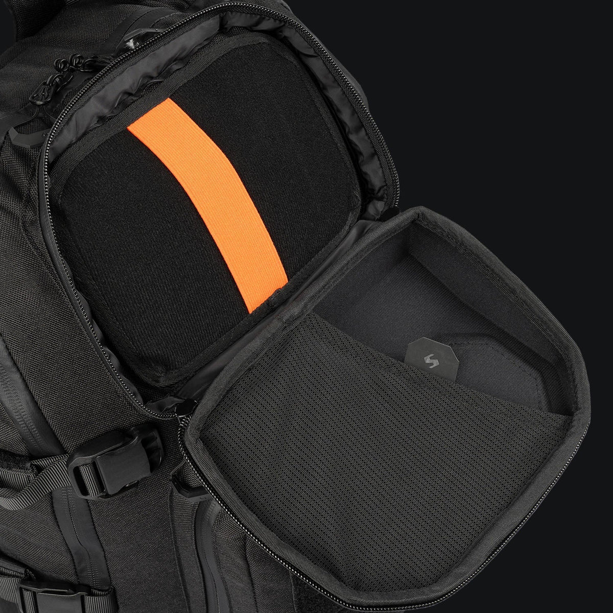 Eine Nahaufnahme des STOIRM 25L Tactical Pack GEN2 von STOIRM zeigt ein gepolstertes Fach mit einem orangefarbenen Gurt und einer Netztasche auf dem Deckel, in der Elektronik oder Zubehör sicher organisiert und geschützt werden können.