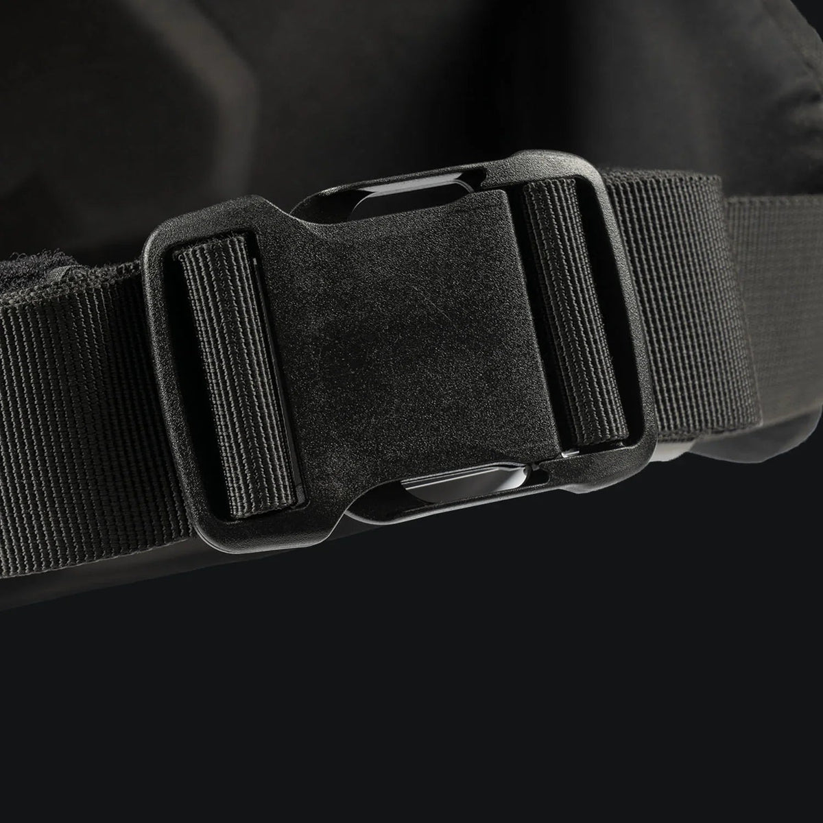 Nahaufnahme einer schwarzen Kunststoffschnalle, die an einem schwarzen Nylongurt befestigt ist und das robuste Design des STOIRM 40L Tactical Pack GEN2 von STOIRM vor einem dunklen Hintergrund hervorhebt.
