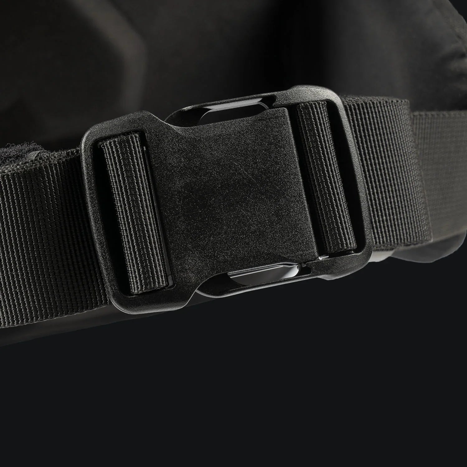 Nahaufnahme einer schwarzen Kunststoffschnalle, die an einem schwarzen Gurt befestigt ist, Teil des STOIRM 40L Tactical Pack GEN2-ideal für Outdoor-Abenteuer, dargestellt vor einem dunklen Hintergrund.