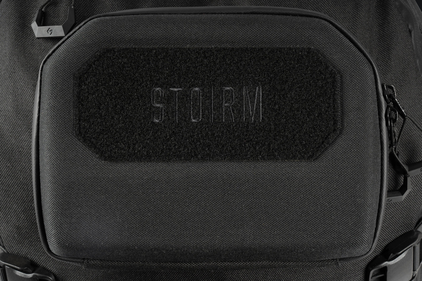 Nahaufnahme des STOIRM 40L Tactical Pack GEN2, ein schwarzer taktischer Rucksack mit einem rechteckigen Aufnäher mit dezent erhabenem "STOIRM" Schriftzug. Hergestellt aus strapazierfähigem Material mit schwarzen Reißverschlüssen ist er perfekt für Outdoor-Abenteuer.