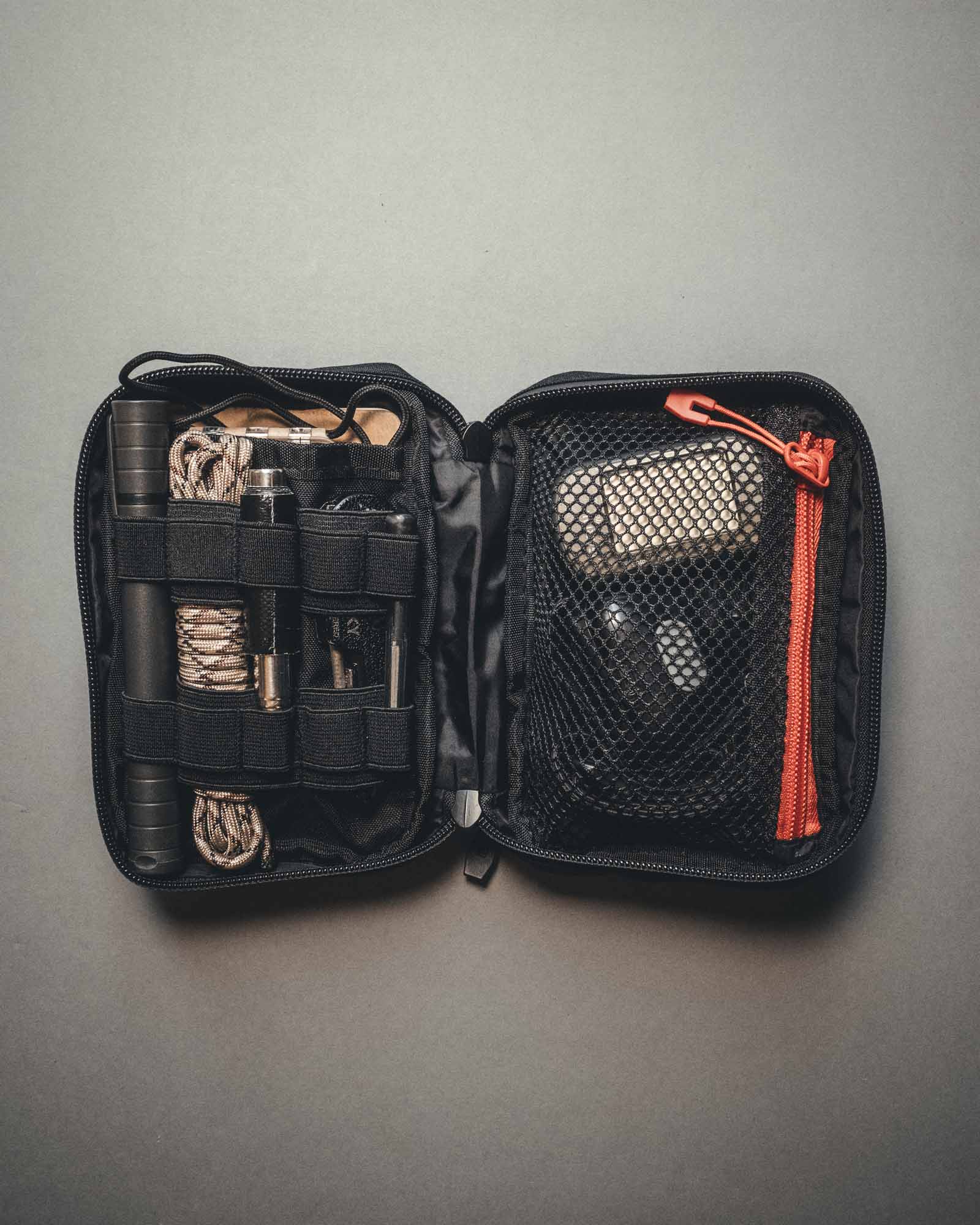 Eine offene schwarze STOIRM Large Pouch V.2 mit Werkzeug-, Seil- und Ausrüstungsfächern auf der linken Seite und einer Netztasche mit rotem Reißverschluss auf der rechten Seite, perfekt als Rucksack Zubehör, dargestellt vor grauem Hintergrund.