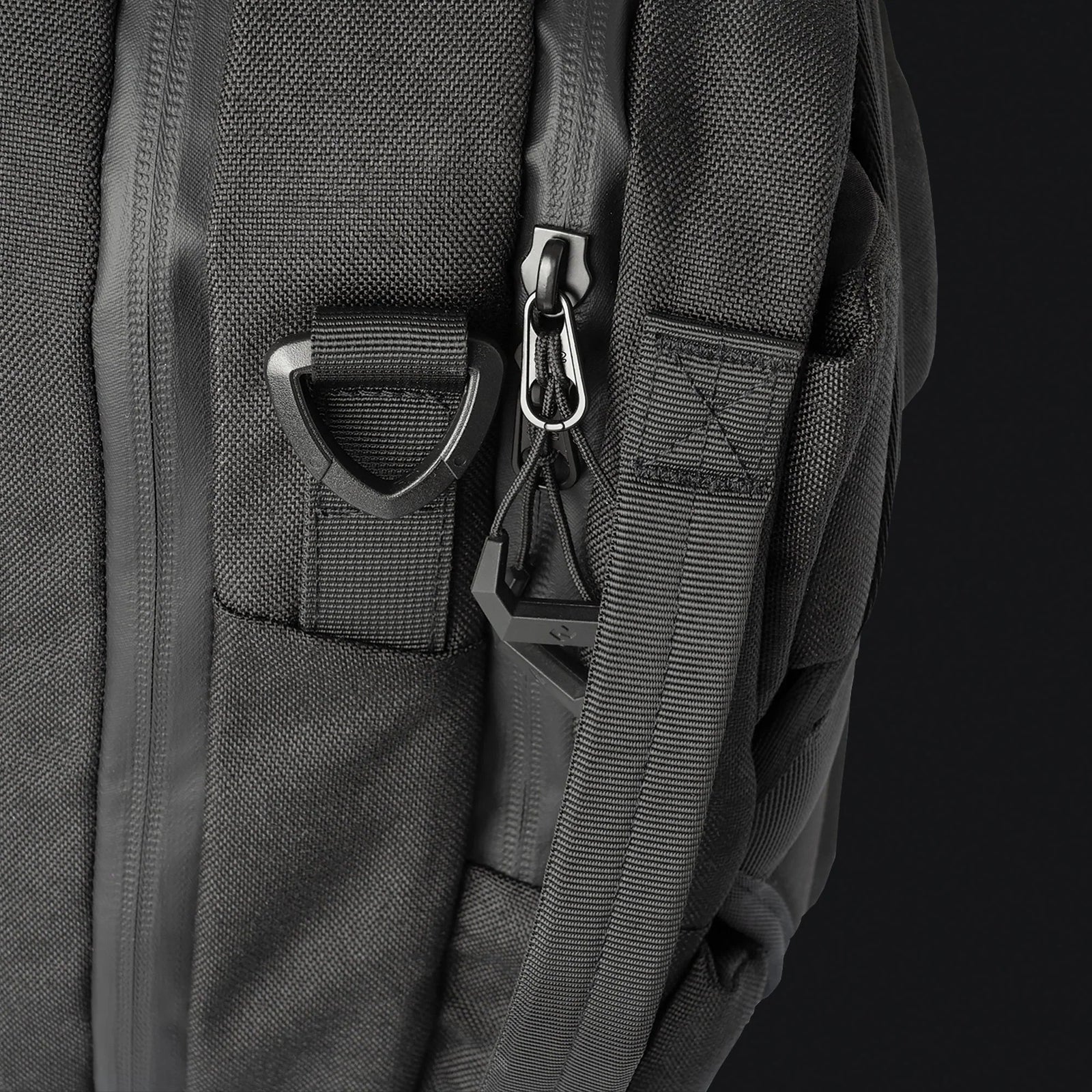 Die Nahaufnahme der STOIRM Messenger Bag von STOIRM zeigt einen robusten Reißverschluss, einen D-Ring aus Kunststoff und einen dreieckigen Riemen. Der strukturierte, strapazierfähige Stoff macht diese wasserfeste Tasche perfekt für den harten Einsatz. Sie verfügt über ein geräumiges Laptopfach für 17 Zoll.
