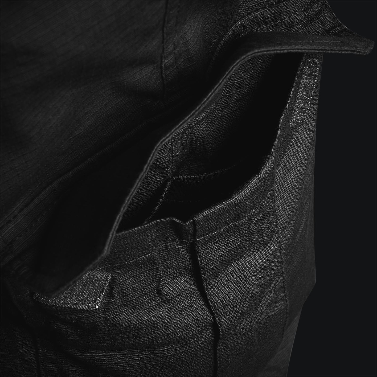 Nahaufnahme einer offenen Tasche aus schwarzem Stoff mit sichtbaren Nähten und Ripstop-Stretchgewebe, mit Details auf der Innenseite und am Rand - zu sehen bei der STOIRM Tactical Trousers Gen2 in Ranger Green.