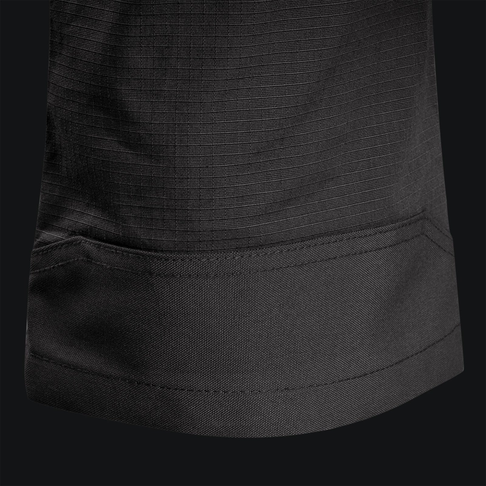 Nahaufnahme des Saums der STOIRM Tactical Trousers Gen2 - Ranger Green von STOIRM, mit präzisen Nähten und strapazierfähigem Ripstop-Stretchgewebe auf schwarzem Hintergrund.