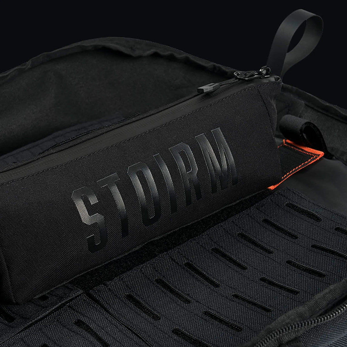 Eine Nahaufnahme der STOIRM Utility Pouch von STOIRM, hergestellt aus strapazierfähigem 500D Nylon mit wasserdichtem Reissverschluss und erhabenem Branding, gezeigt in einer offenen schwarzen Tasche mit organisierten Fächern.