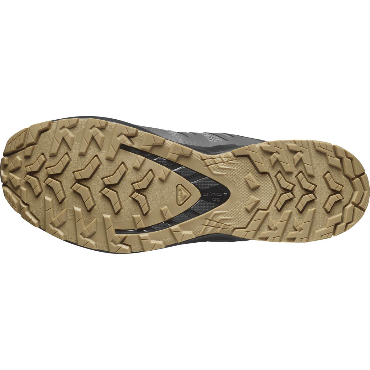 Das Bild zeigt die hellbraune Gummilaufsohle des SALOMON FORCES XA PRO FORCES - Clrock / Black / Gum, die ein robustes, multidirektionales Profil für Traktion auf verschiedenen Oberflächen aufweist. Das Dynafit-Logo erscheint in der Mitte der Sohle.