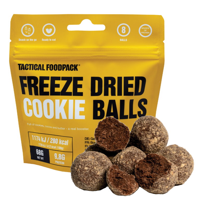 Ein gelber, wiederverschließbarer Beutel mit der Aufschrift TACTICAL FOODPACK Cookie Balls steht aufrecht und zeigt runde, schokoladige, gefriergetrocknete Kekskugeln vor. Auf der Verpackung sind Nährwertangaben und Piktogramme abgebildet.
