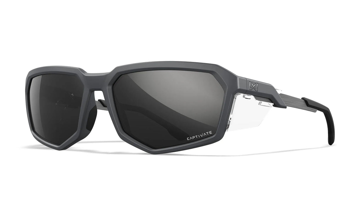 Die WILEY X Sonnenbrille RECON ist eine mattschwarze, kantige Outdoor-Brille mit großen, dunkel getönten Gläsern, geometrischem Rahmen, CAPTIVATE-Schriftzug auf dem linken Glas und dezentem Branding an den Bügeln.