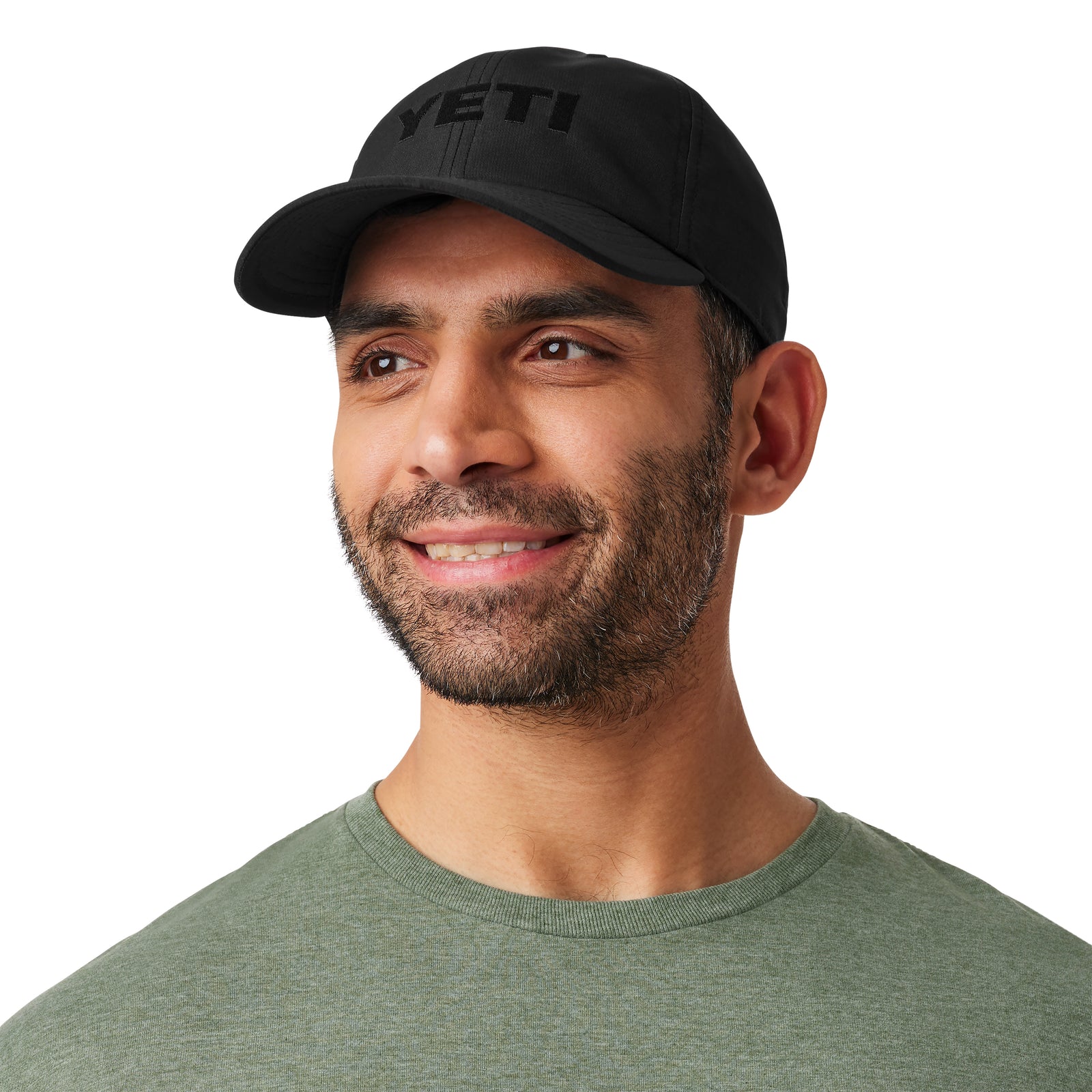 Ein Mann mit kurzem Bart und Schnurrbart lächelt leicht. Er trägt eine schwarze YETI® Baseballkappe von YETI und ein hellgrünes T-Shirt vor einem schlichten weißen Hintergrund, der den klassischen Stil dieser Kappe hervorhebt.