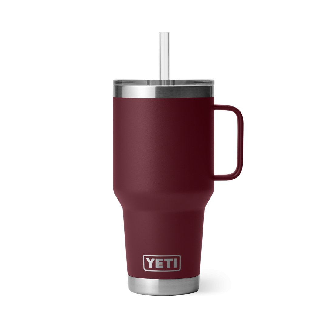 Ein YETI® Becher Rambler 35 Oz Straw Mug in Wild Vine Red aus Edelstahl mit Henkel, Klarsichtdeckel und Strohhalm steht auf weißem Hintergrund. Das YETI-Logo ist am unteren Rand des isolierten Markenbechers sichtbar.