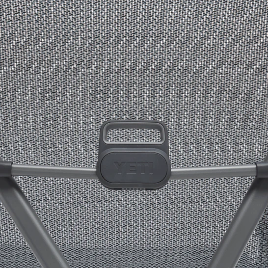 Nahaufnahme der Rückenlehne des YETI® Campingstuhls Trailhead - Charcoal, die einen schwarzen Kunststoffgriff mit geprägtem YETI-Branding und kantigen Metallrahmenstützen an der Unterseite zeigt.
