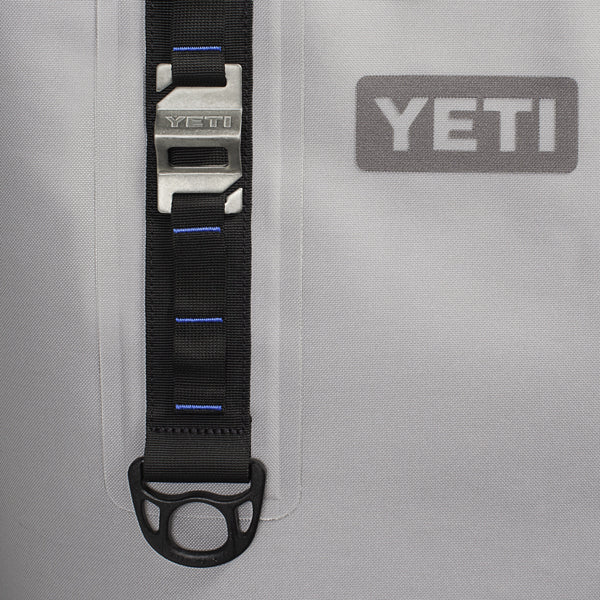 Nahaufnahme einer grauen YETI-Tasche mit Metallschnalle, schwarzem Gurt mit blauen Nähten und dem YETI-Logo - kompatibel mit dem MOLLE-System zur Aufnahme von Zubehör wie dem YETI® Flaschenöffner - Molle Bottle Opener von YETI.