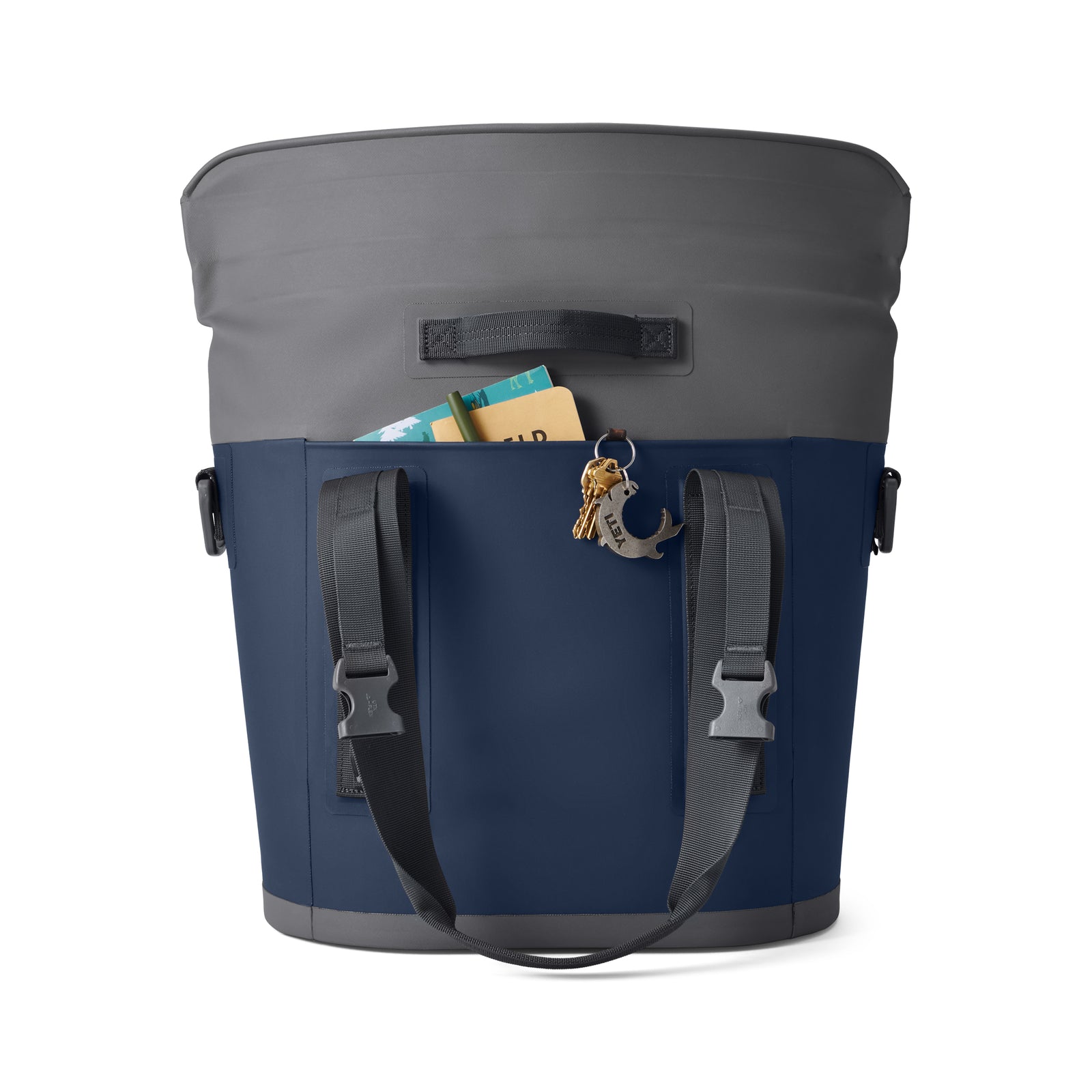 Eine geräumige marineblaue und graue Tasche mit schwarzen Trägern, einer Außentasche für ein Buch und eine Brieftasche sowie einem Schlüsselanhänger - ideal für den Transport mit Ihrer YETI® Hopper M15 Soft Cooler - Navy von YETI.