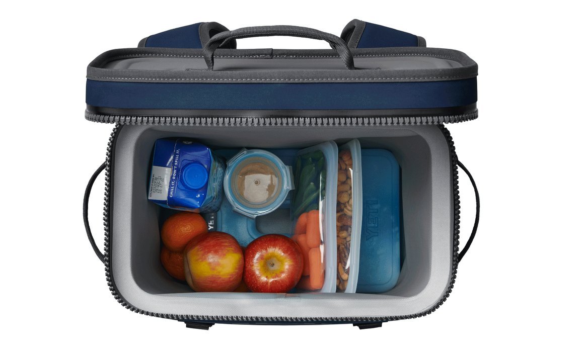 Draufsicht auf eine geöffnete blaue Brotzeittasche mit Äpfeln, Orangen, Babykarotten, Nüssen, einem Hummus-Behälter, einem YETI® Kühlakku Ice Sheet Large, einem Getränkekarton und einem Kunststoffbehälter mit hellblauem Deckel.