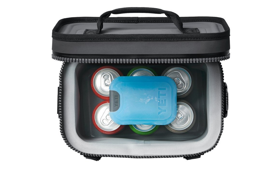 Draufsicht auf eine YETI-Soft-Side-Kühlbox mit sechs Dosen und einer blauen YETI® Kühlakku-Eisplatte Small, wobei die Dosen um die Eisplatte im isolierten Fach angeordnet sind - perfekt für Fans von Hochleistungs-Kühlboxen.