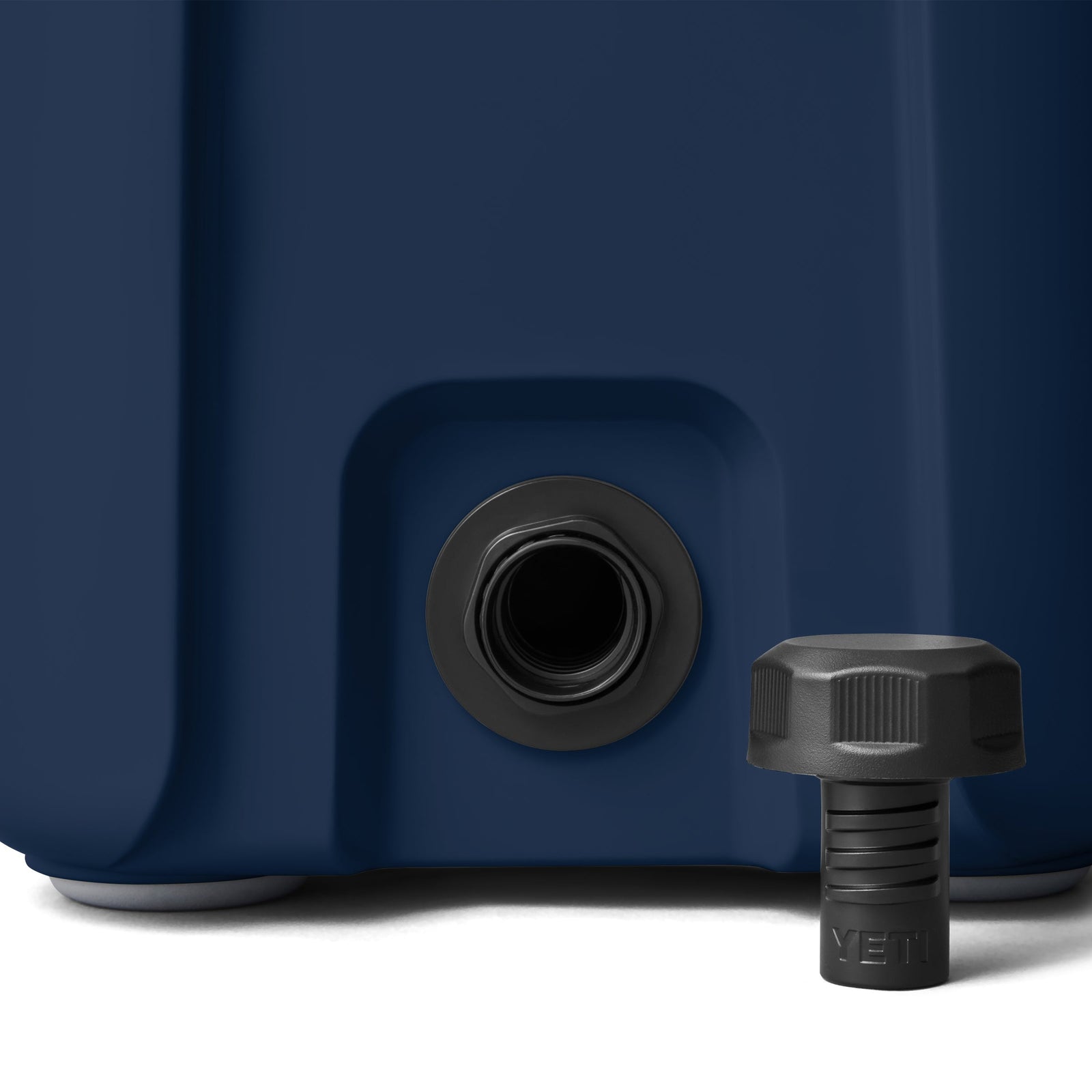 Nahaufnahme der Ablassöffnung einer marinefarbenen YETI® Kühlbox Roadie 15, mit entfernter schwarzer Ablassschraube, die neben der Öffnung angebracht ist.