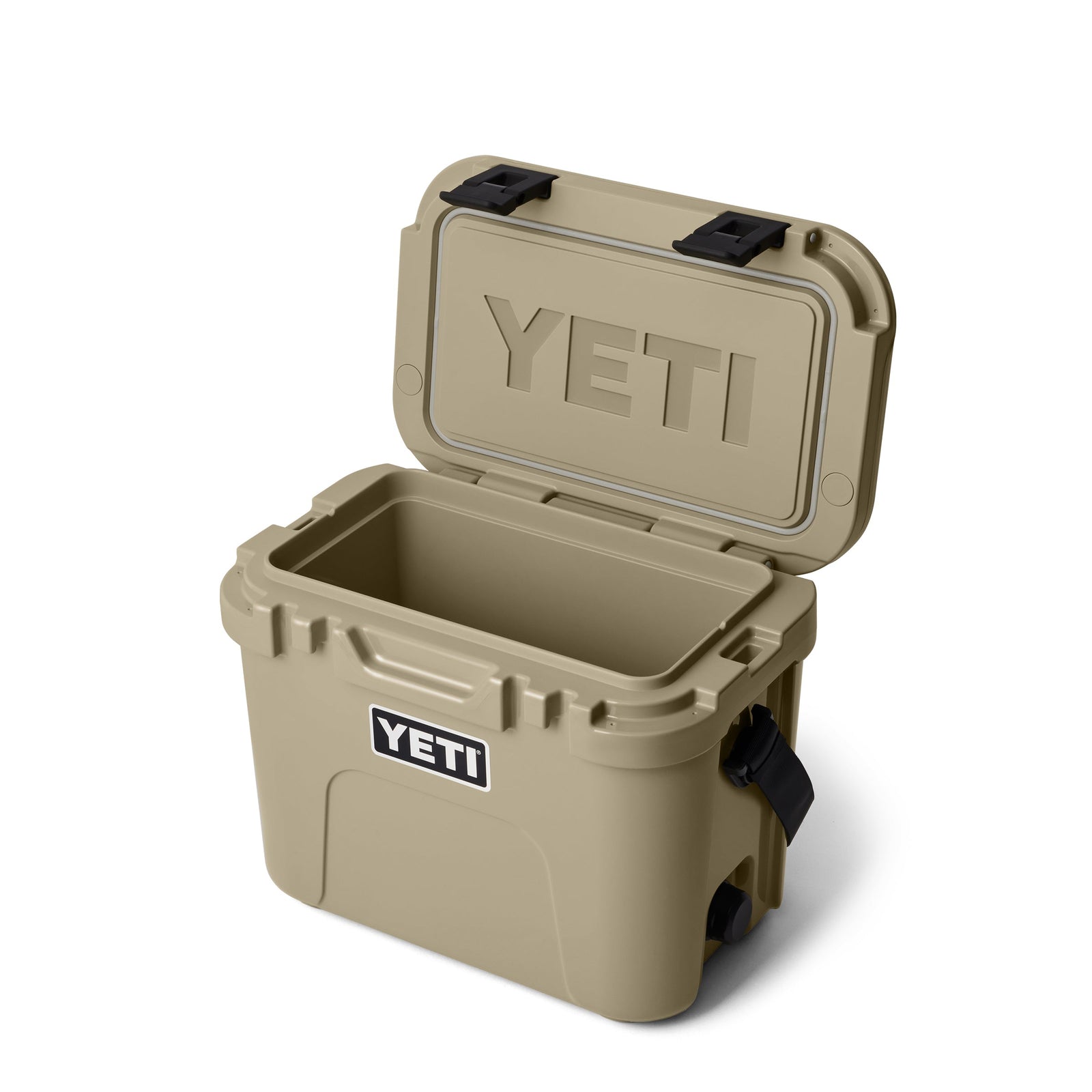Die YETI® Kühlbox Roadie 15 - Tan ist mit geöffnetem Deckel abgebildet, der den leeren, isolierten Innenraum zeigt. Das YETI-Logo befindet sich auf der Vorderseite und auf der Innenseite des Deckels. Große schwarze Seitengriffe und eine robuste Konstruktion zeichnen diese tragbare Kühlbox aus.