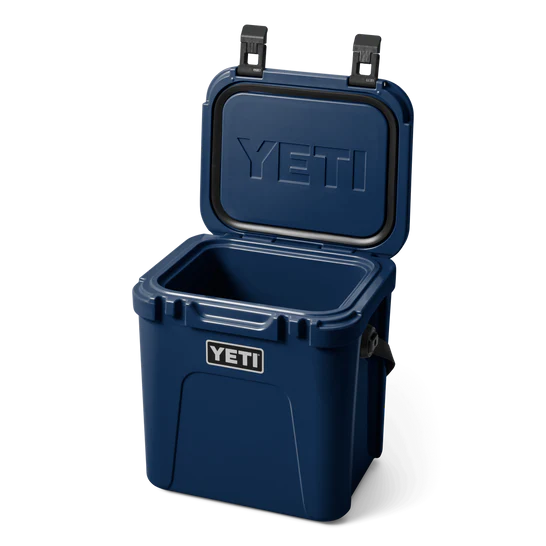 Die YETI® Kühlbox Roadie 24 in Navy ist offen dargestellt mit dem geprägten YETI-Logo auf dem Deckel und einer Frontplakette. Sie verfügt über PermaFrost Isolierung für langanhaltende kalte Lagerung.