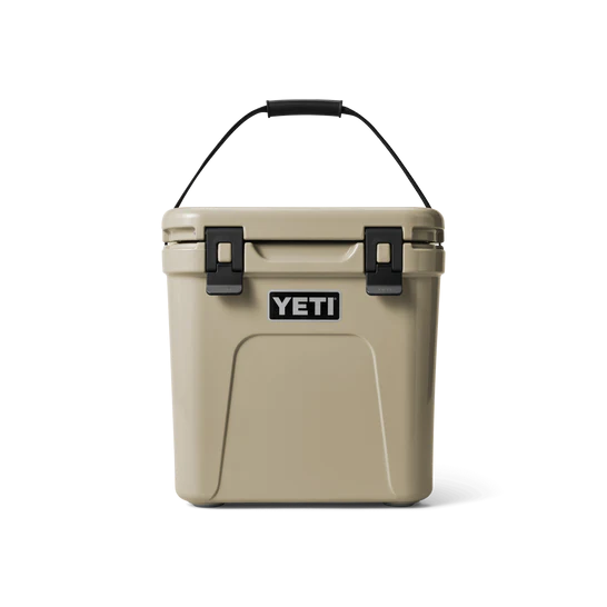 Die YETI® Kühlbox Roadie 24 in Tan ist mit einem stabilen Griff und zwei schwarzen Frontverschlüssen ausgestattet und wird auf einem schlichten weißen Hintergrund gezeigt.
