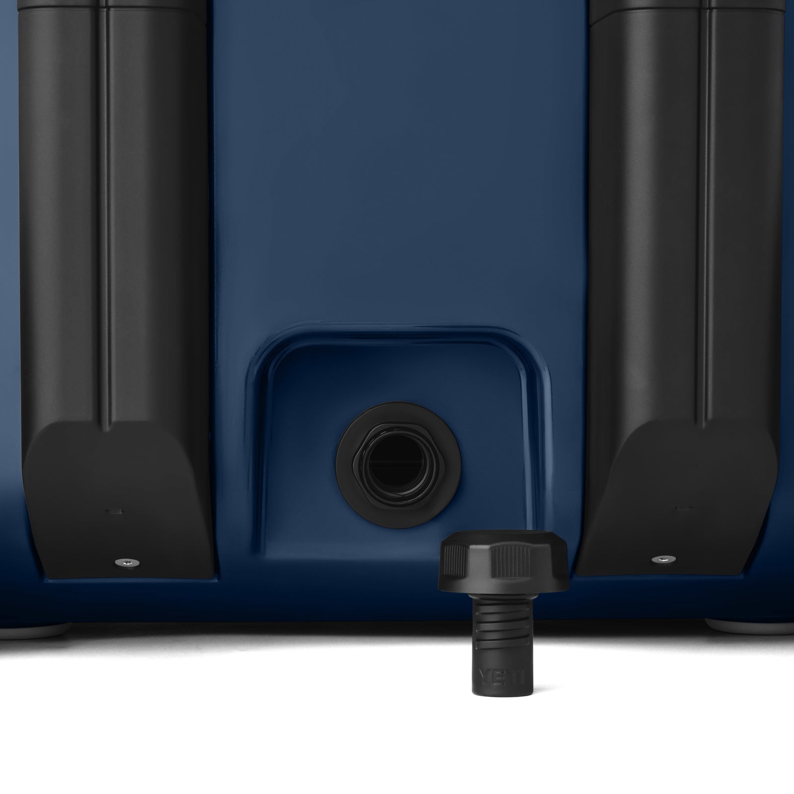 Nahaufnahme der YETI® Kühlbox Roadie 32 - Navy: eine dunkelblaue, robuste Kühlbox von YETI mit schwarzen zylindrischen Seitenaufsätzen und einer zentralen Abflussöffnung mit Gewinde und schwarzem Stopfen auf weißem Hintergrund.