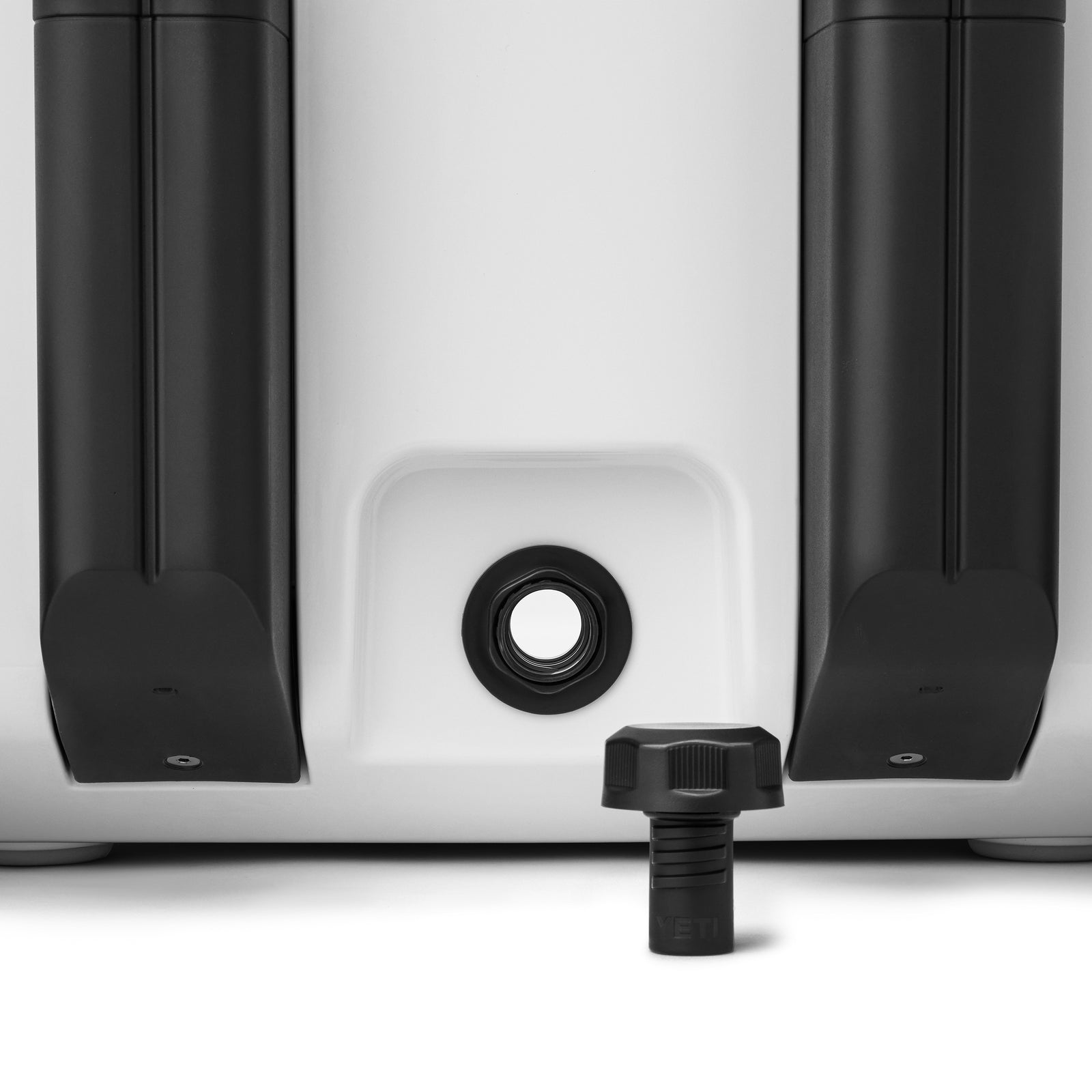 Nahaufnahme des Bodens der weißen YETI® Kühlbox Roadie 32 mit zwei schwarzen Rädern und einer zentralen schwarzen Ablassschraube, die abgeschraubt und unter der Öffnung platziert wird - perfekt für Ihr nächstes YETI-Abenteuer.