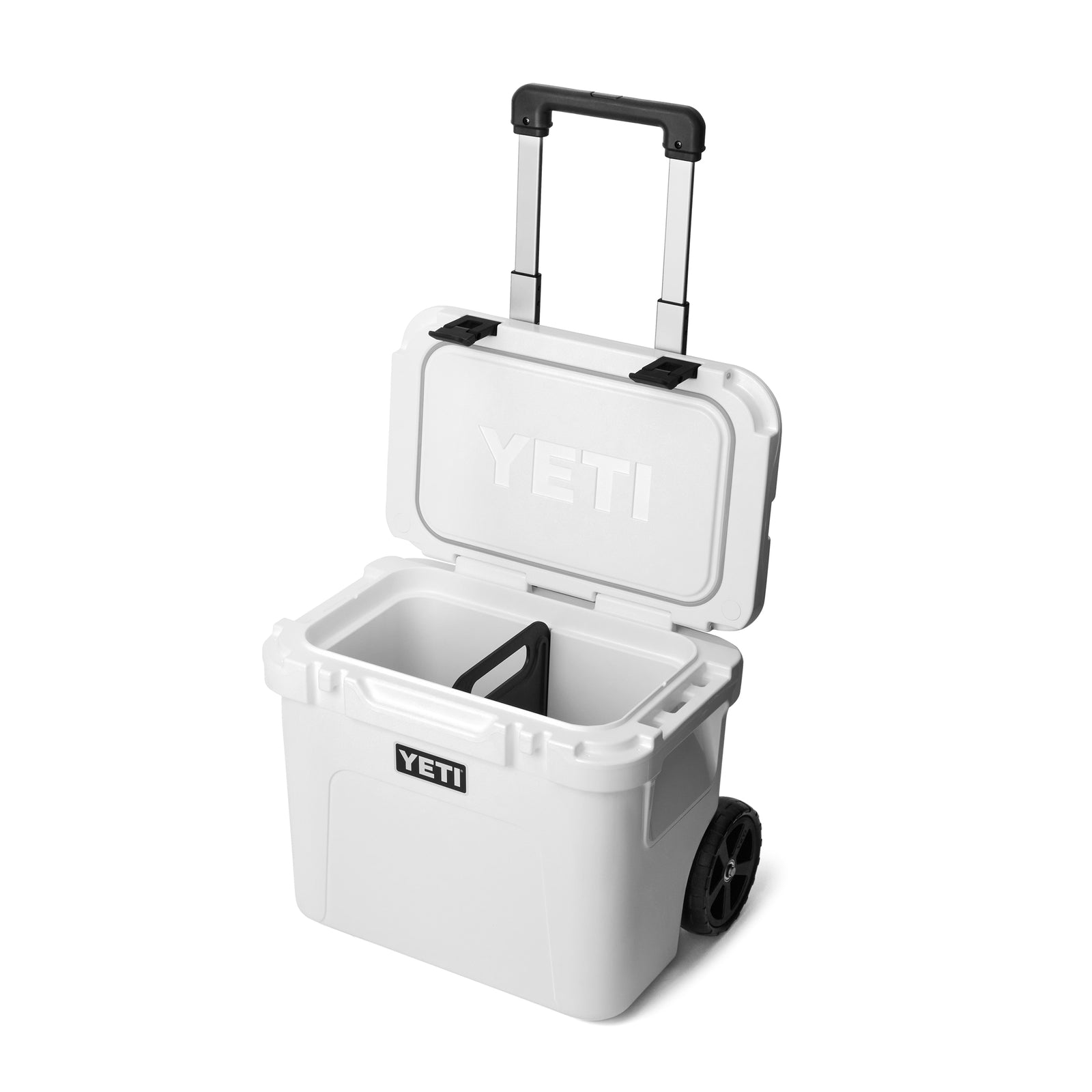 Die weiße YETI® Kühlbox Roadie 32 hat robuste Räder, einen schwarzen aufrechten Griff und einen offenen Deckel, der den leeren Innenraum mit einer Trennwand freigibt. Das YETI-Logo ist gut sichtbar auf der Vorderseite und der Innenseite des Deckels angebracht.
