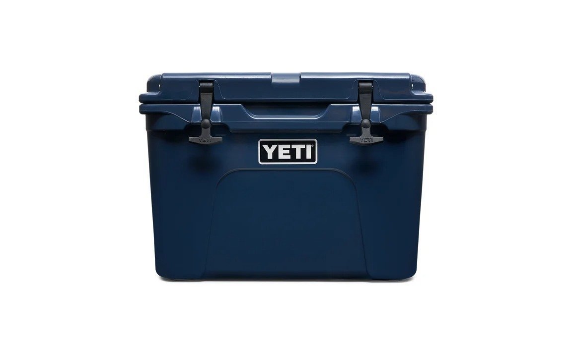 Die YETI® Kühlbox Tundra 35 in Navy verfügt über zwei schwarze Frontverschlüsse und ein zentriertes weißes und schwarzes YETI-Logo sowie eine robuste rotationsgeformte Konstruktion. Die Kühlbox ist vor einem schlichten weißen Hintergrund abgebildet.