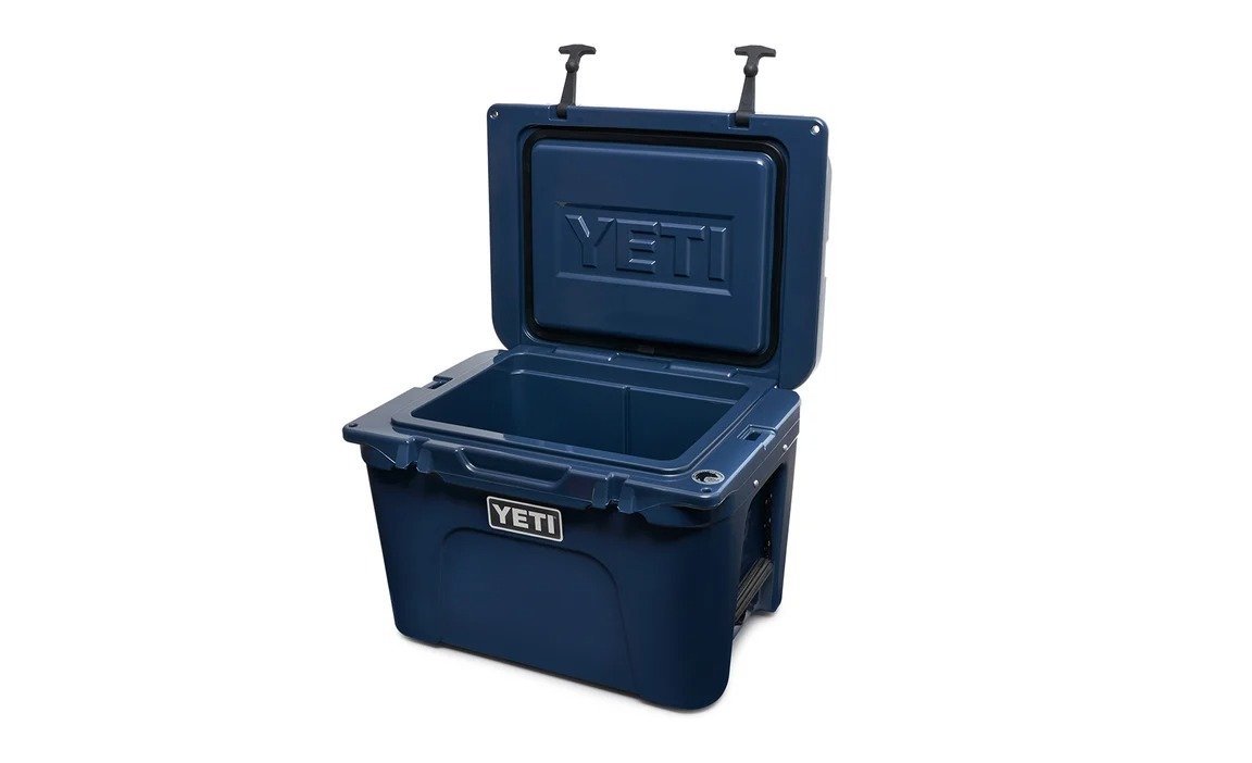 Die YETI® Kühlbox Tundra 35 - Navy wird geöffnet gezeigt und offenbart ihren geräumigen, isolierten Innenraum und die rotationsgeformte Konstruktion. Stabile Griffe und ein robustes Design zeigen das YETI-Logo auf der Vorderseite und der Innenseite des Deckels.