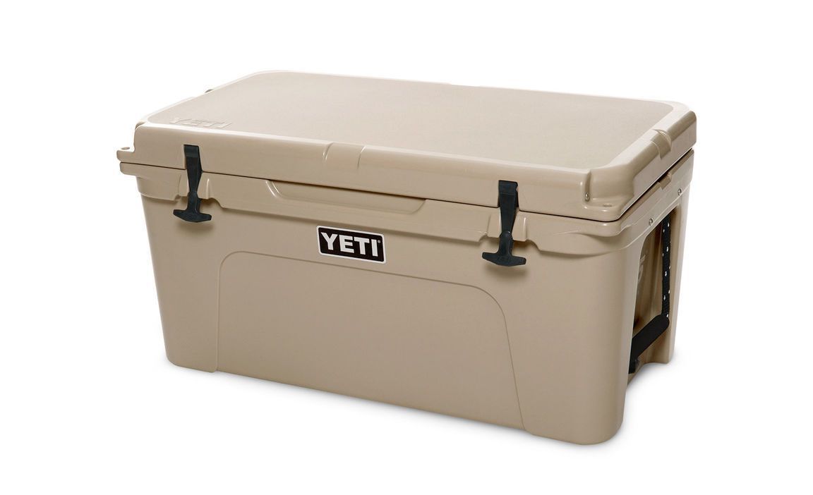Eine hellbraune YETI® Kühlbox Tundra 65 mit geschlossenem Deckel, stabilen Seitengriffen und schwarzen Frontverschlüssen von YETI, abgebildet vor einem weißen Hintergrund.