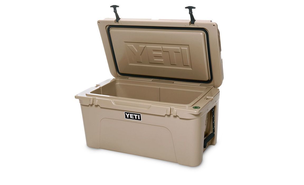 Die YETI® Kühlbox Tundra 65 in Tan verfügt über einen geräumigen isolierten Innenraum, schwarze Seitengriffe und einen sichtbaren YETI-Schriftzug auf der Vorderseite und dem Innendeckel - perfekt für Ihren nächsten Campingausflug.