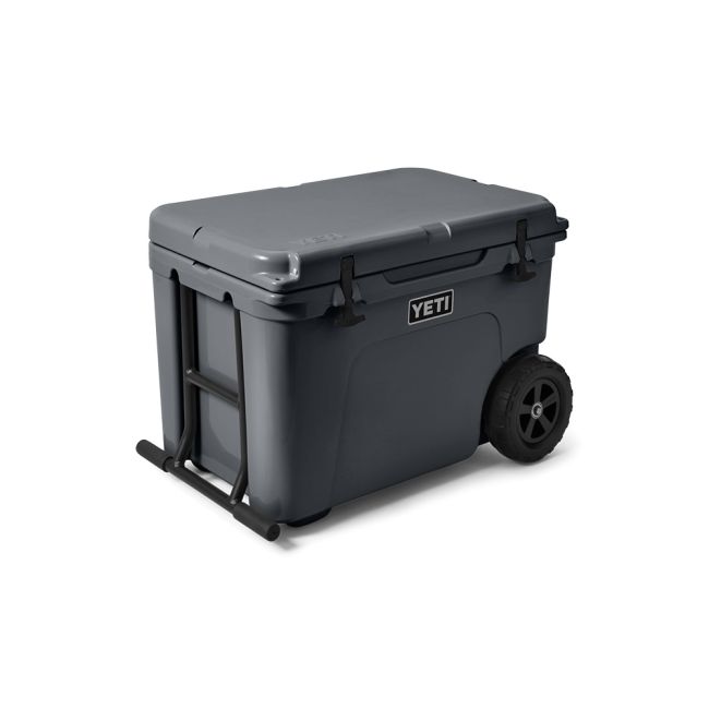 Die YETI® Kühlbox Tundra Haul - Charcoal ist eine große, dunkelgraue Kühlbox mit einem aufklappbaren Deckel, stabilen Seitengriffen und zwei schwarzen Rädern für den einfachen Transport. Das YETI-Logo erscheint auf der Vorderseite dieser rollbaren Kühlbox.
