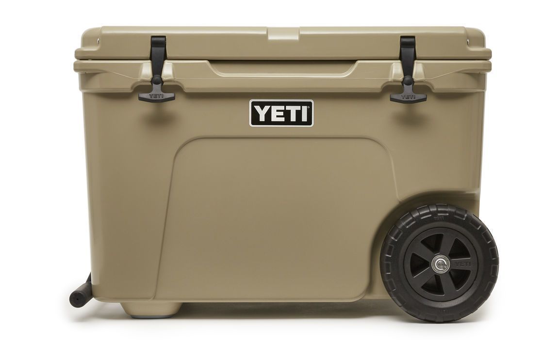 Die YETI® Kühlbox Tundra Haul - Tan ist eine Hartschalenkühlbox mit zwei schwarzen Verschlüssen und großen schwarzen Rädern, die für einen einfachen Transport konzipiert ist.