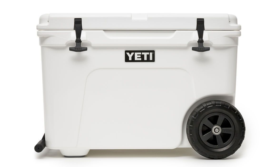 Die YETI® Kühlbox Tundra Haul - White hat ein schwarzes Logo auf der Vorderseite, zwei große schwarze Räder auf einer Seite und zwei schwarze Gummiriegel am Deckel für einen sicheren Verschluss.